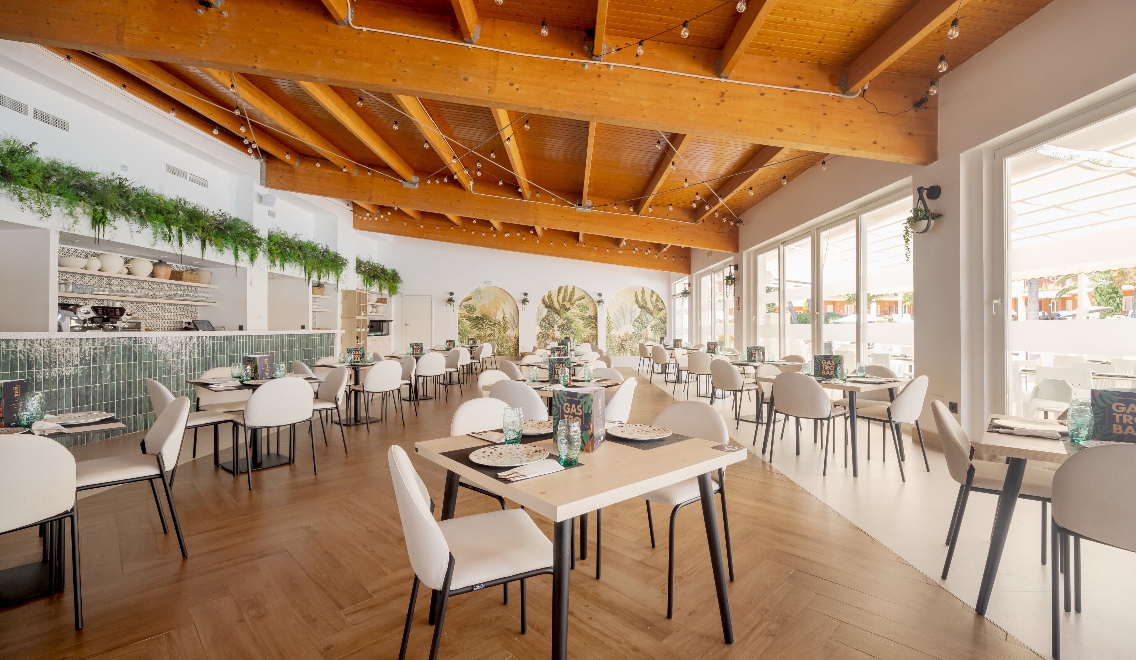 Un restaurante espacioso con vigas de madera, sillas blancas y grandes ventanales.