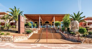 A hotel entrance with a covered staircase, palm trees, and a stone monument. - Aparthotel ILUNION Sancti Petri (Chiclana de la Frontera)