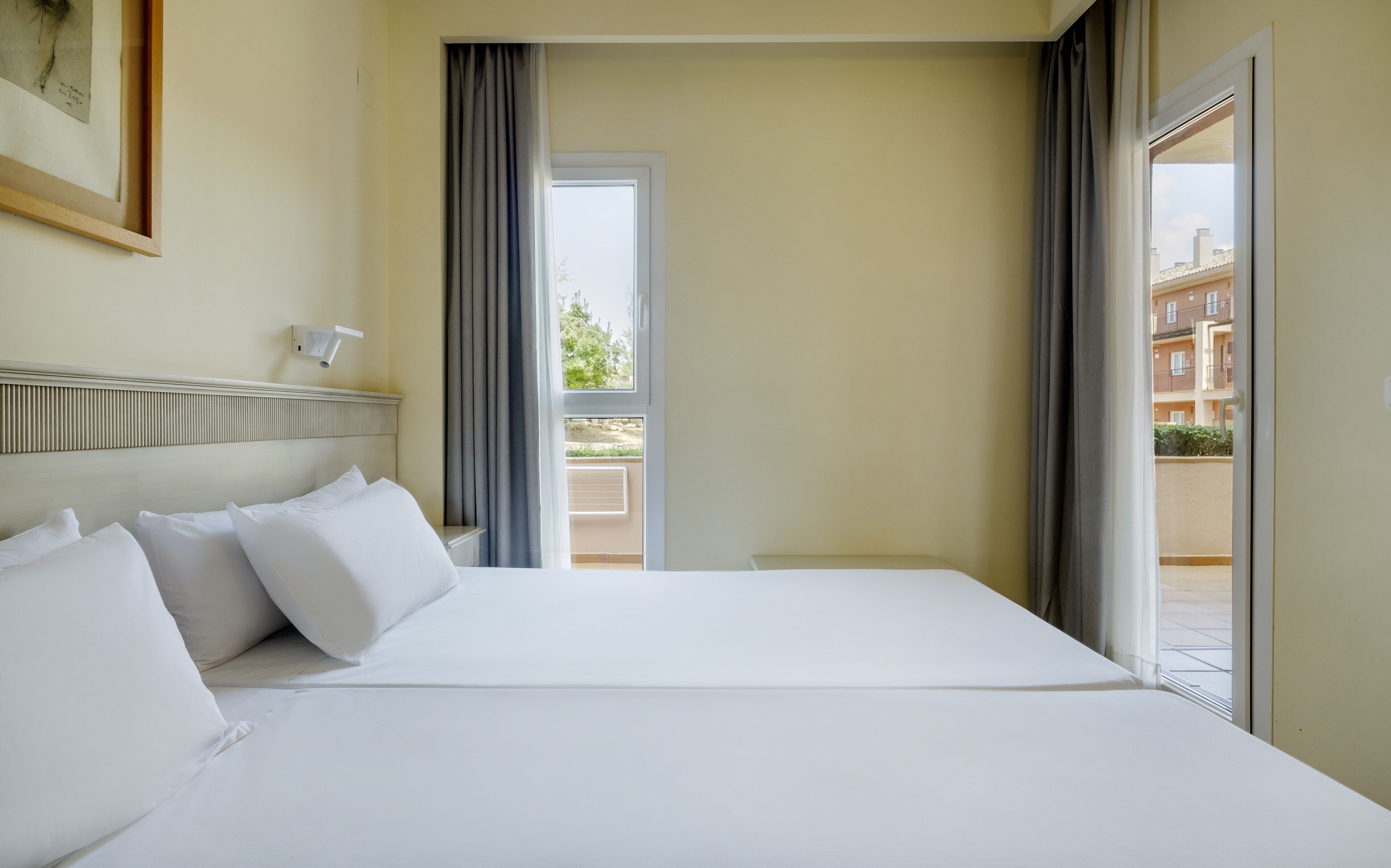 A hotel room with a large bed, a headboard, a window with curtains, and a view of the outside.