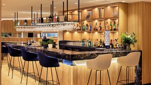 Zona de bar con encimera de mármol, varios taburetes y una variedad de botellas y vasos.