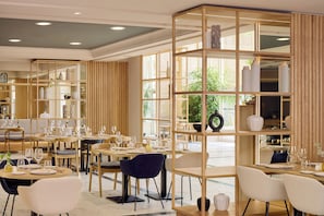 Un comedor moderno con varias mesas y sillas, separadores de madera y luz natural gracias a amplias ventanas.