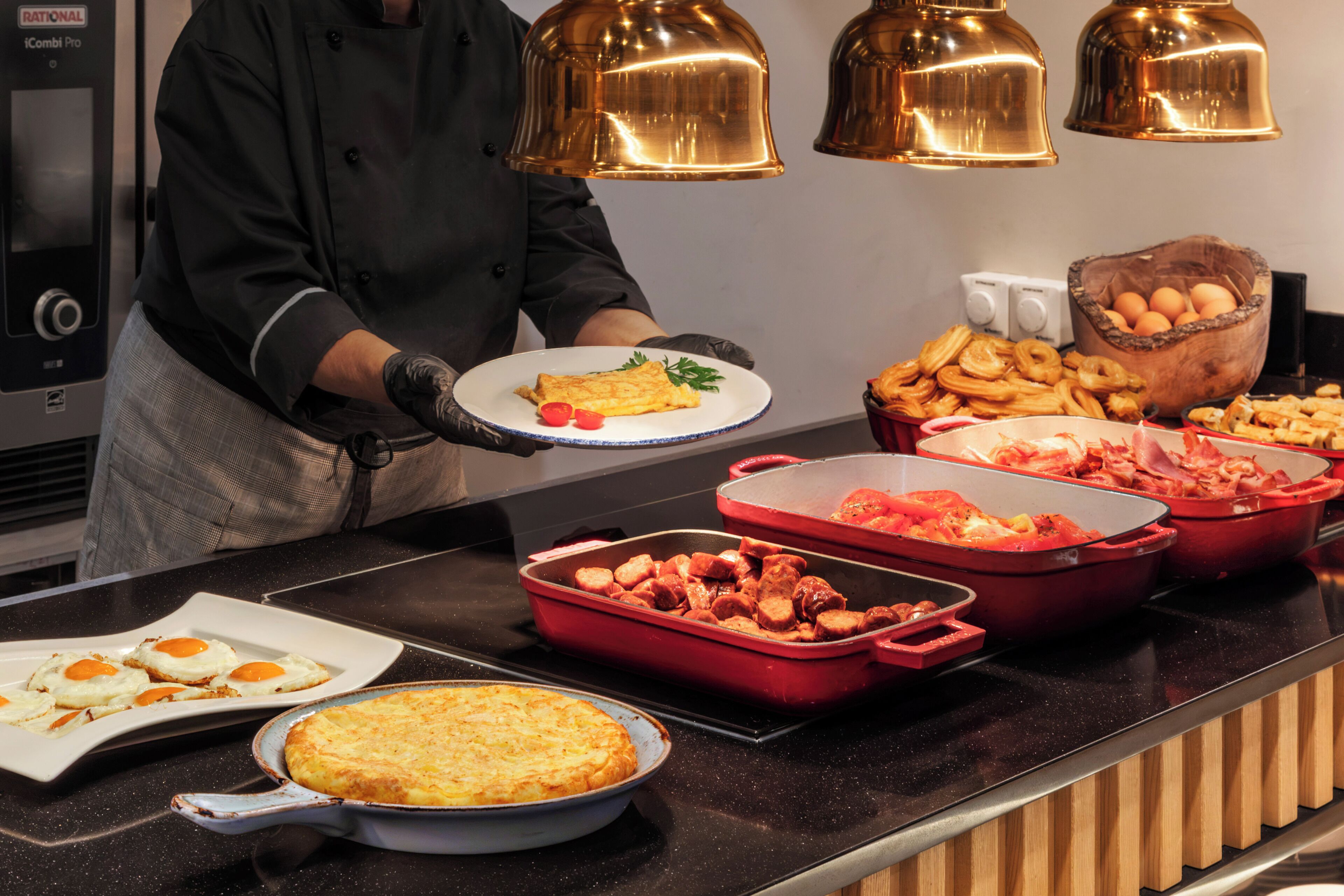 A buffet setup with various food items, including a plate with eggs, a casserole dish, and red chafing dishes with meat.