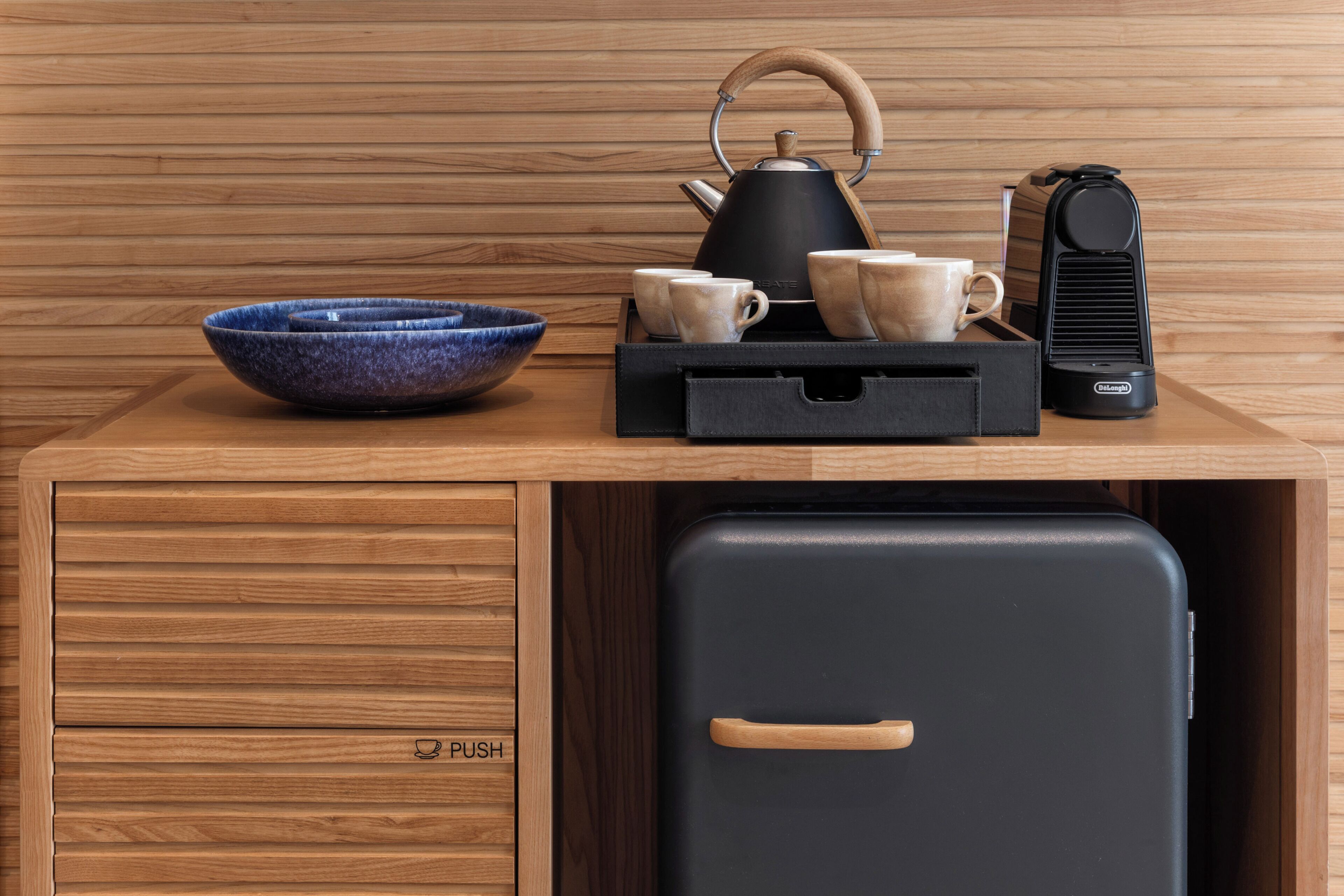 Una mesa de madera con una tetera negra, un tazón azul y una cafetera negra.