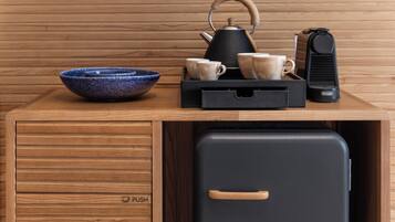 Una mesa de madera con una tetera negra, un tazón azul y una cafetera negra.