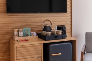 Una kitchenette compacta con un televisor montado en la pared, una cafetera y un hervidor sobre la encimera.