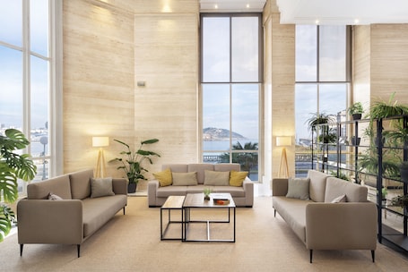A spacious living area with a beige sofa set, a coffee table, and large windows offering a view of a cityscape and mountains.