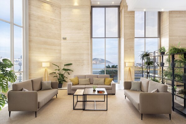 Amplia sala de estar con sofá color beige, una mesa de centro y ventanas grandes con vistas a la ciudad y montañas.