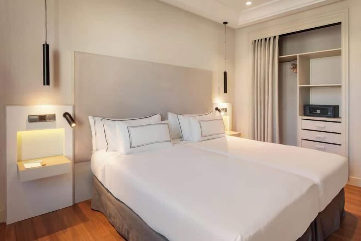 Ein modernes Hotelzimmer mit einem großen Bett, Nachttischen, einem Kleiderschrank und einer Deckenleuchte.