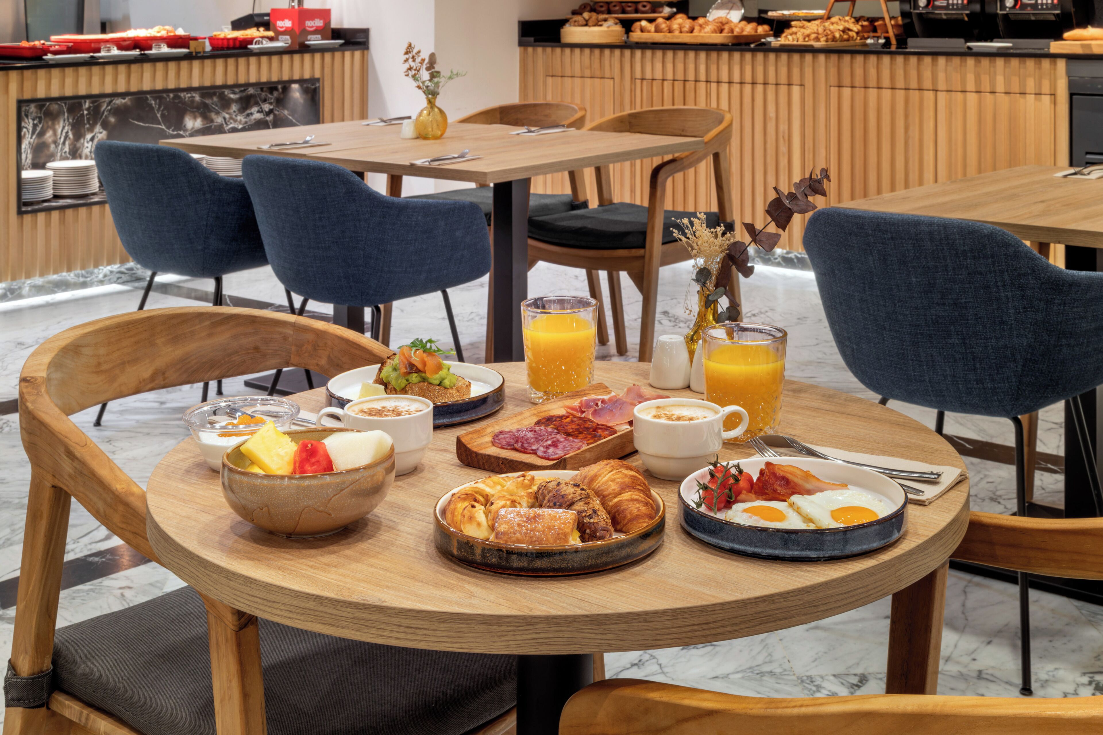 A breakfast setting with a variety of food items, including eggs, pastries, and fruit, on a wooden table.