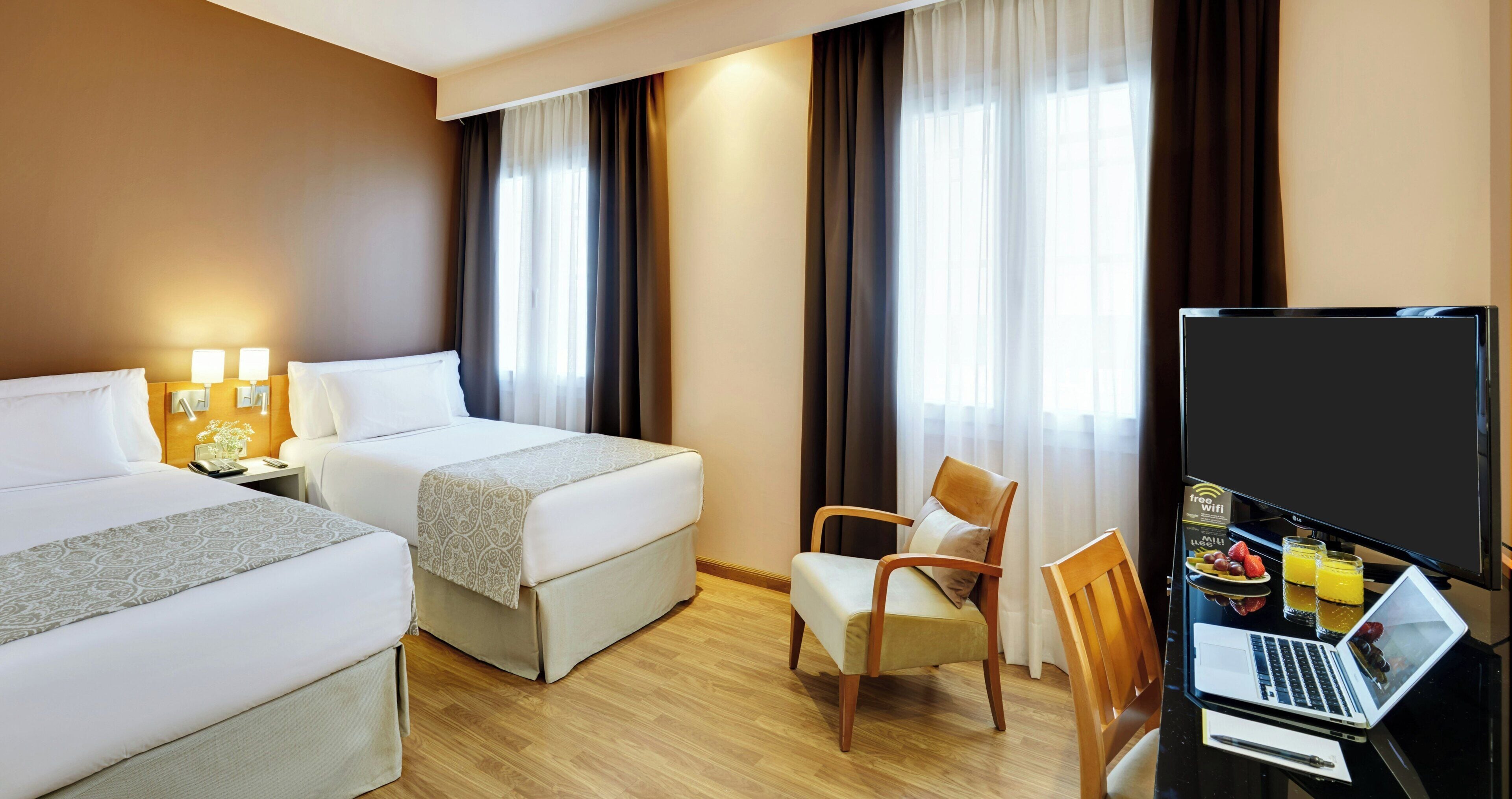 Een hotelkamer met twee bedden, een bureau met een laptop, een stoel en een televisie.