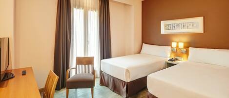 A hotel room with two beds, a desk, a chair, and a window with curtains.