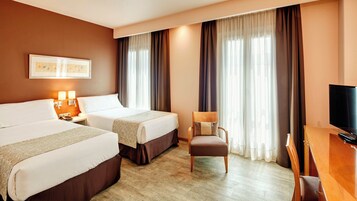 Une chambre d’hôtel avec deux lits, une chaise, un bureau avec une télévision et un tableau au mur.