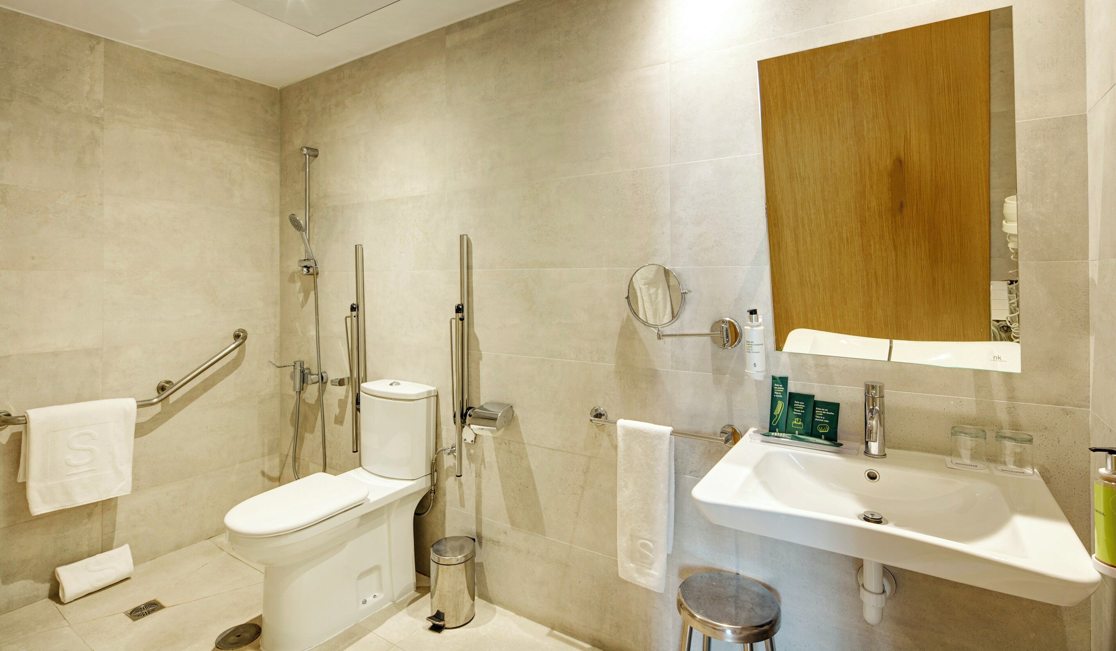 A modern bathroom with a toilet, bidet, shower, sink, and a wooden cabinet.