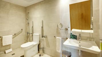 A modern bathroom with a toilet, bidet, shower, sink, and a wooden cabinet.