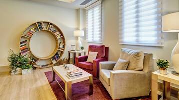 A living room with a round bookshelf, a red armchair, a beige sofa, a coffee table, and a lamp.