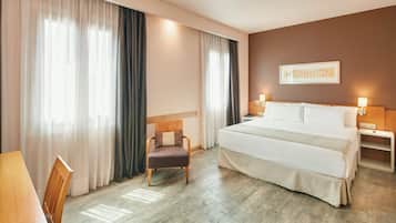 Una habitación de hotel con una cama grande, una silla, un escritorio y una mesita de noche con lámparas.