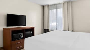 A hotel room with a bed, a flat-screen TV, a minibar, and a window with curtains.