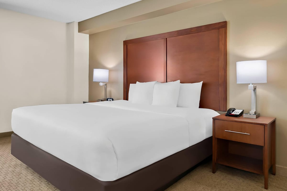A hotel room with a large bed, two bedside tables with lamps, a clock, and a phone on one of the tables.