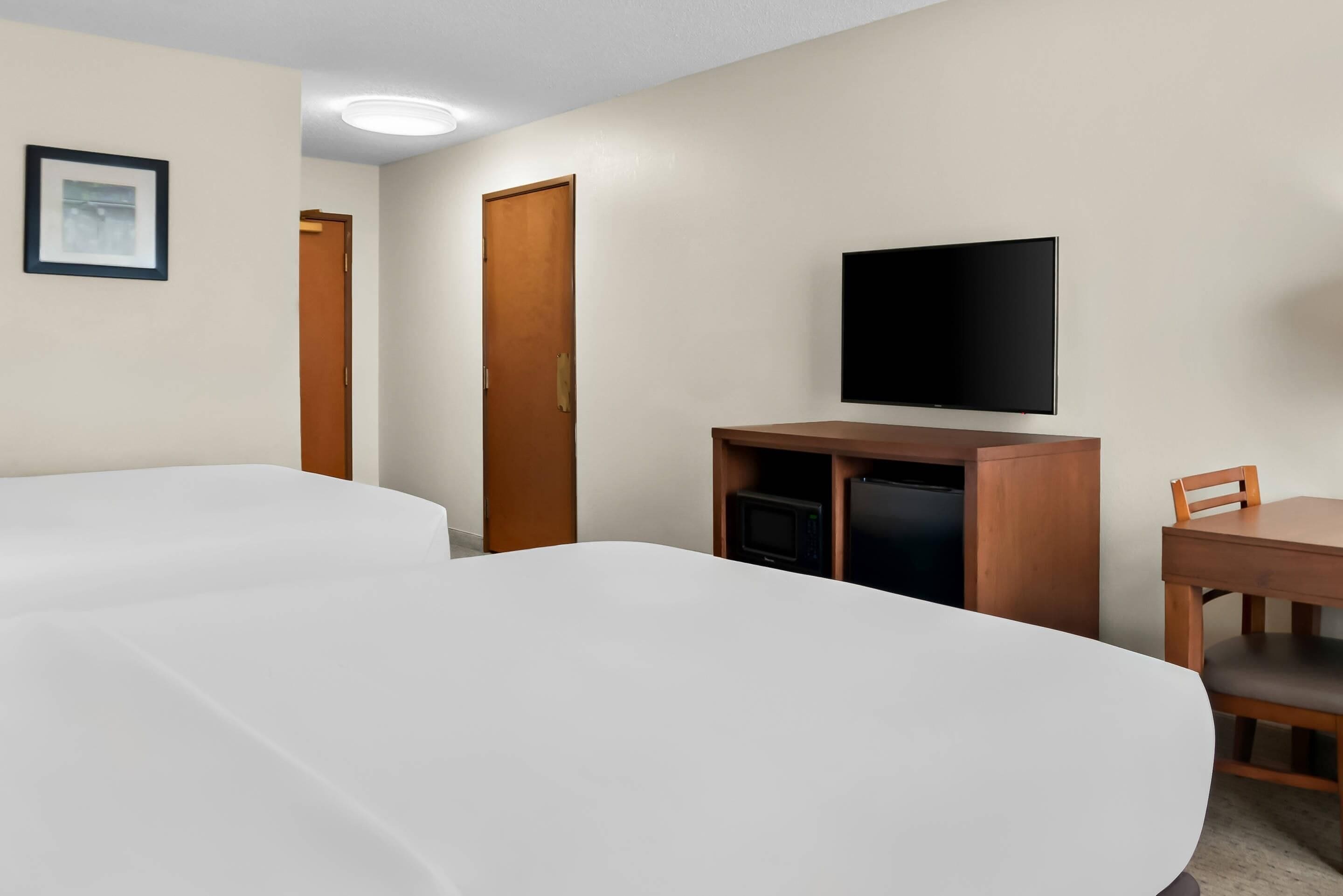A hotel room with two beds, a TV, a desk, and a chair.