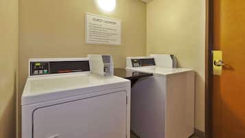 A guest laundry area with two washing machines and dryers, a sign with laundry instructions, and a door to the right.