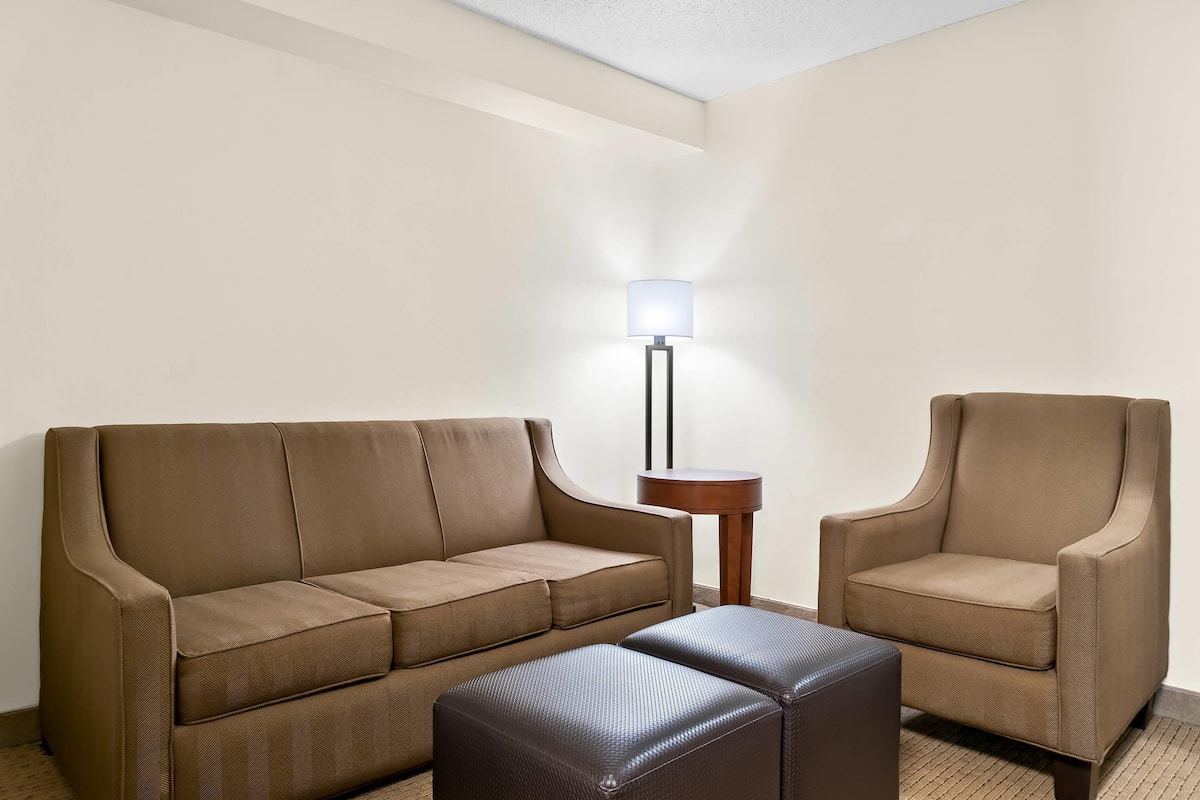 A room with a brown sofa, a matching armchair, and a small side table with a lamp.