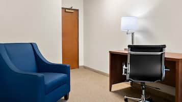 Una habitación con un sillón azul, un escritorio con una silla de oficina negra, una lámpara y una puerta de madera.