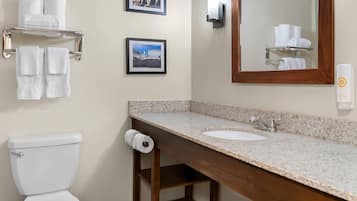 A bathroom with a toilet, a sink, a mirror, and towel racks with folded towels.