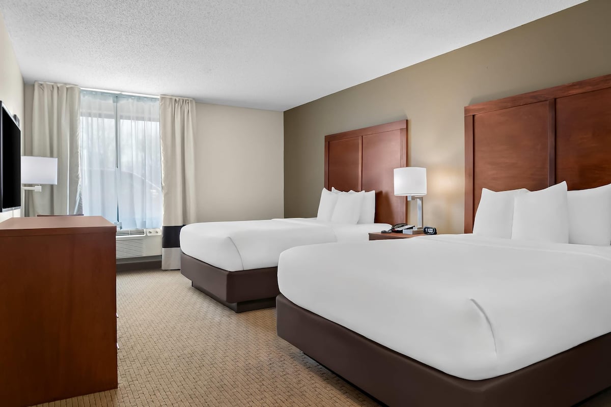 A hotel room with two beds, a desk, a TV, and a window with curtains.