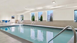 An indoor swimming pool with clear water, a metal ladder, and a seating area with chairs and tables. - Comfort Inn & Suites Taylor - Detroit (Taylor)