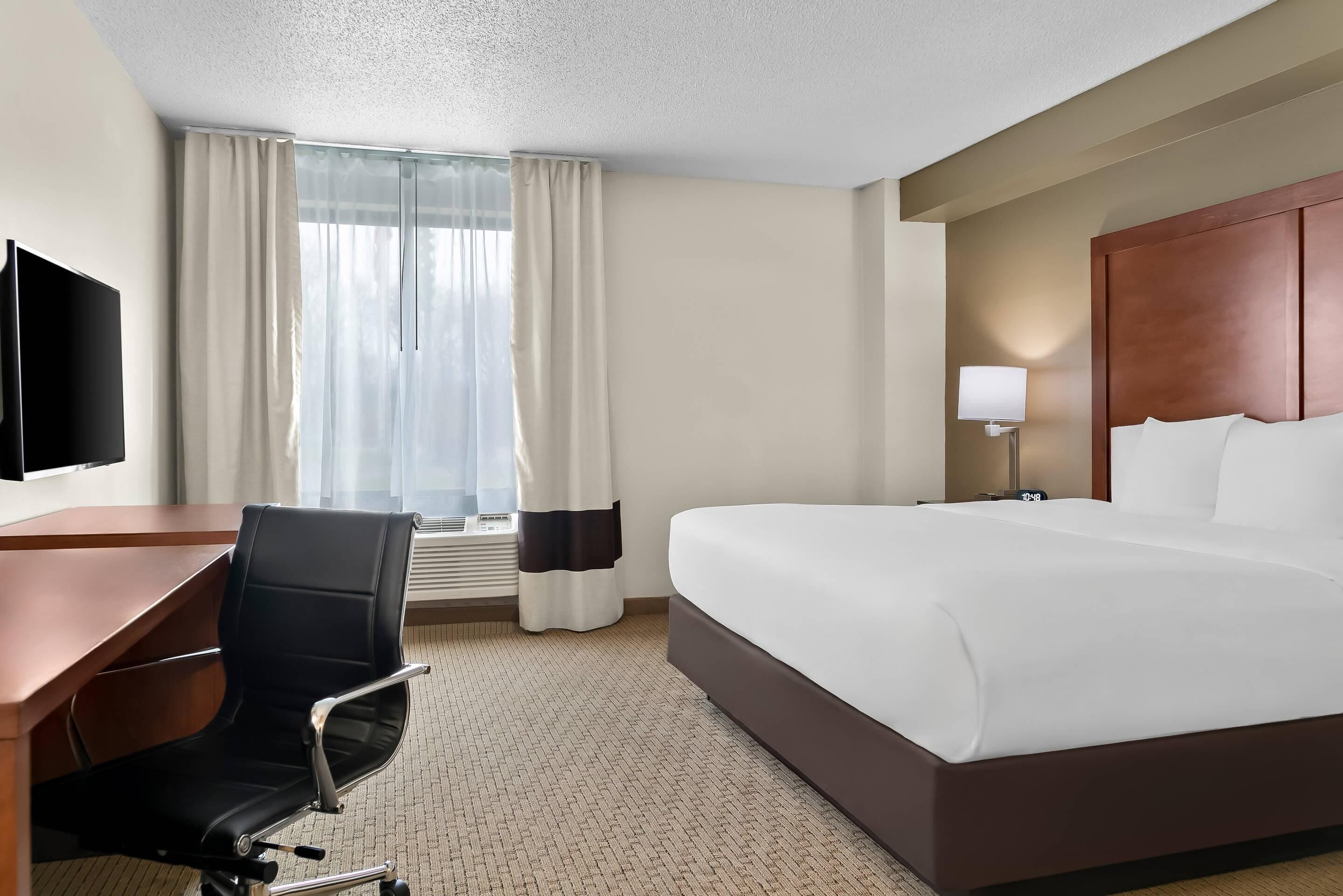 Une chambre d’hôtel équipée d’un lit, d’un bureau, d’une chaise, d’une télévision et d’une fenêtre avec des rideaux.