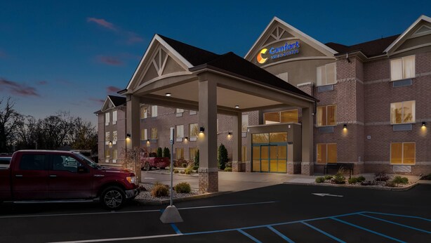 A hotel with a covered entrance, a red pickup truck parked outside, and a clear sky. - Comfort Inn & Suites Taylor - Detroit (Taylor)