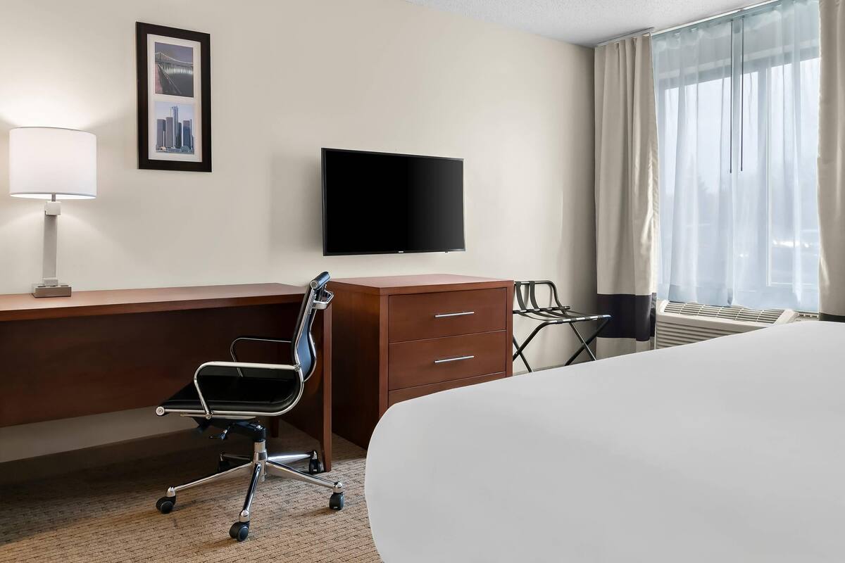 A hotel room with a bed, desk, chair, TV, and window with curtains.