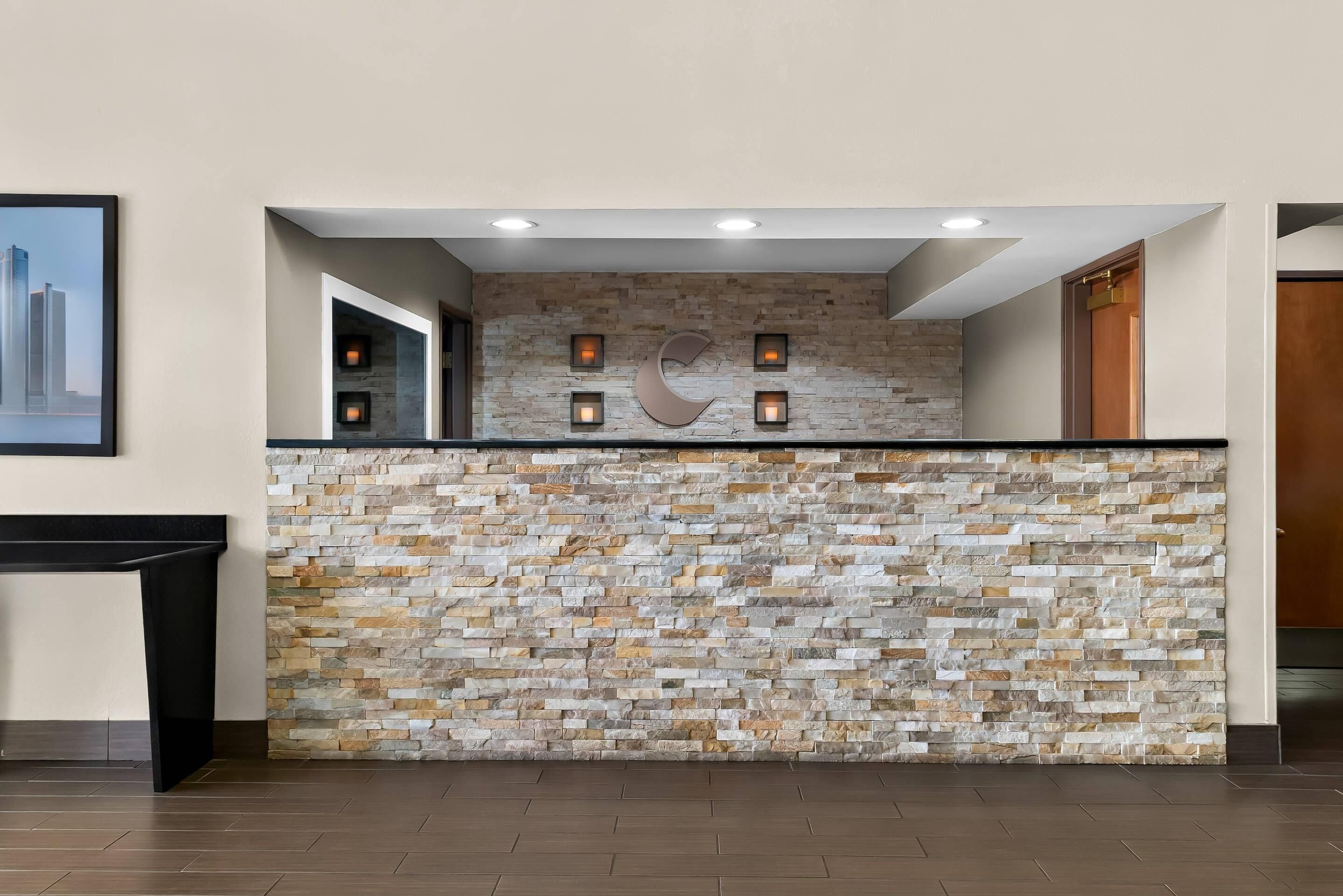 Un área de recepción con pared de piedra, iluminación empotrada y una vista urbana enmarcada.