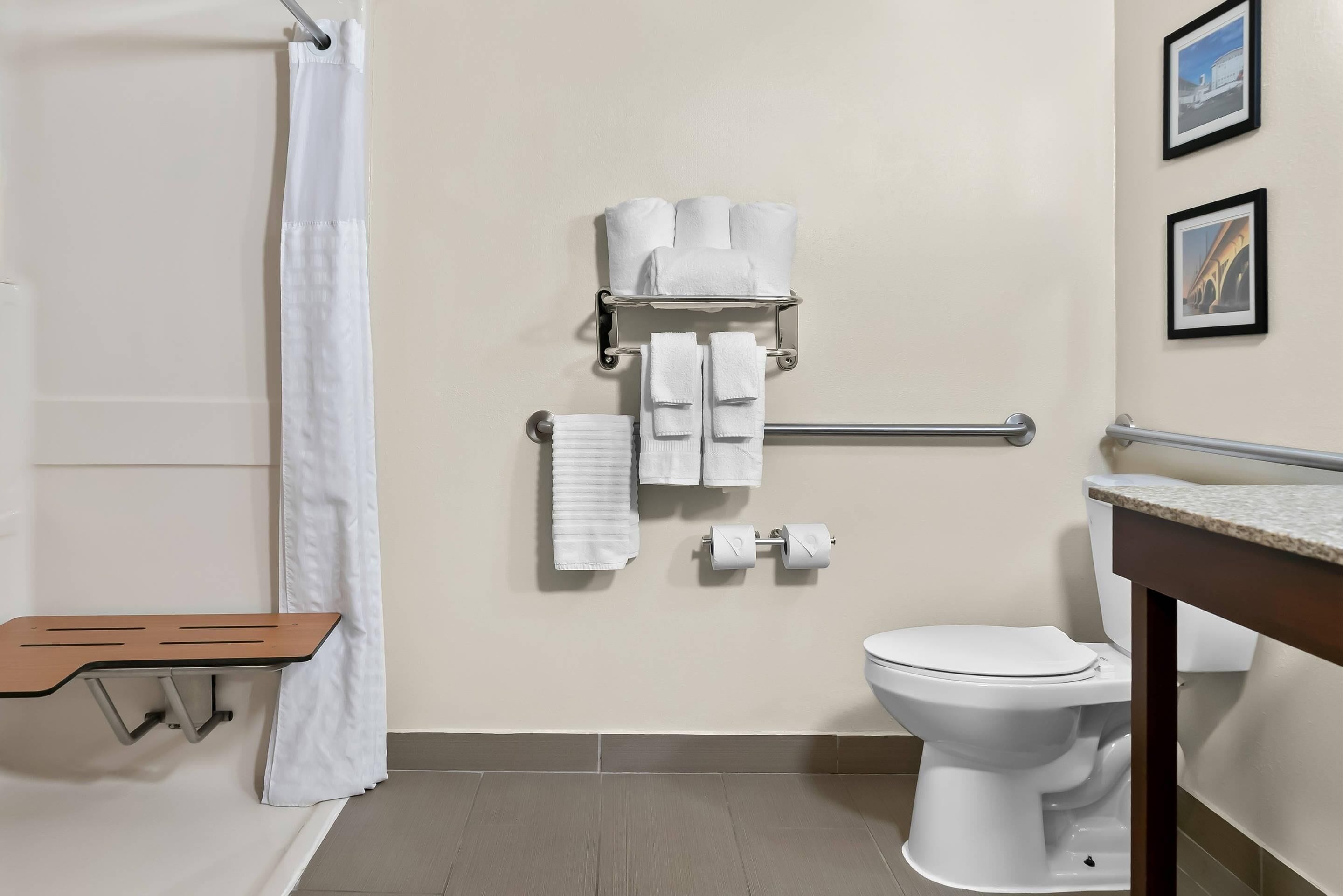 A bathroom with a shower, toilet, towel rack, and a wooden bench.