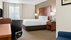 A hotel room with a bed, desk, chair, bedside table, lamp, and a framed picture on the wall. - Comfort Inn & Suites Taylor - Detroit (Taylor)