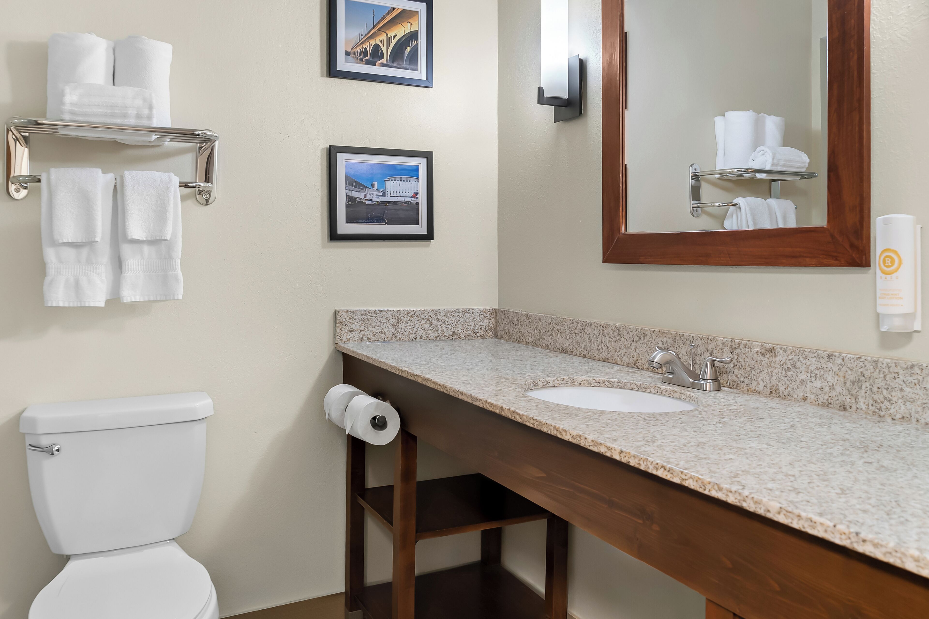 A bathroom with a toilet, sink, towel rack, and framed pictures on the wall.