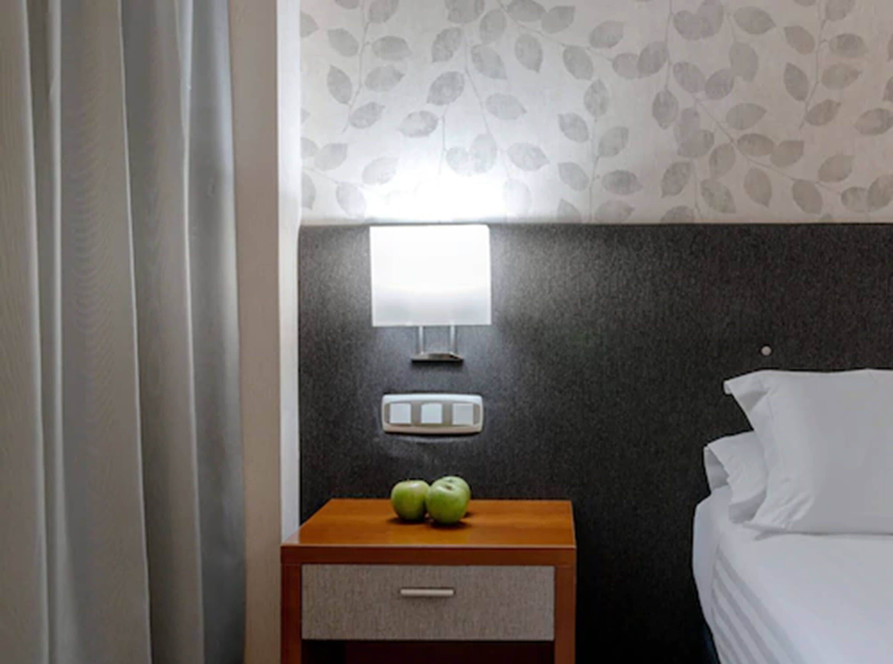 A hotel room with a bed, a nightstand with a lamp, and a wall with a leaf pattern.
