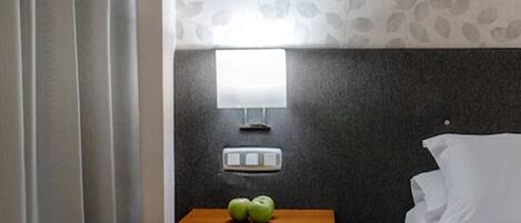 A hotel room with a bed, a nightstand with a lamp, and a wall with a leaf pattern.