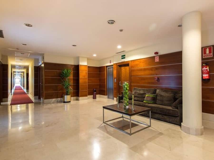 Un vestíbulo de hotel con alfombra roja, paneles de madera, una mesa de centro de vidrio y un sofá.