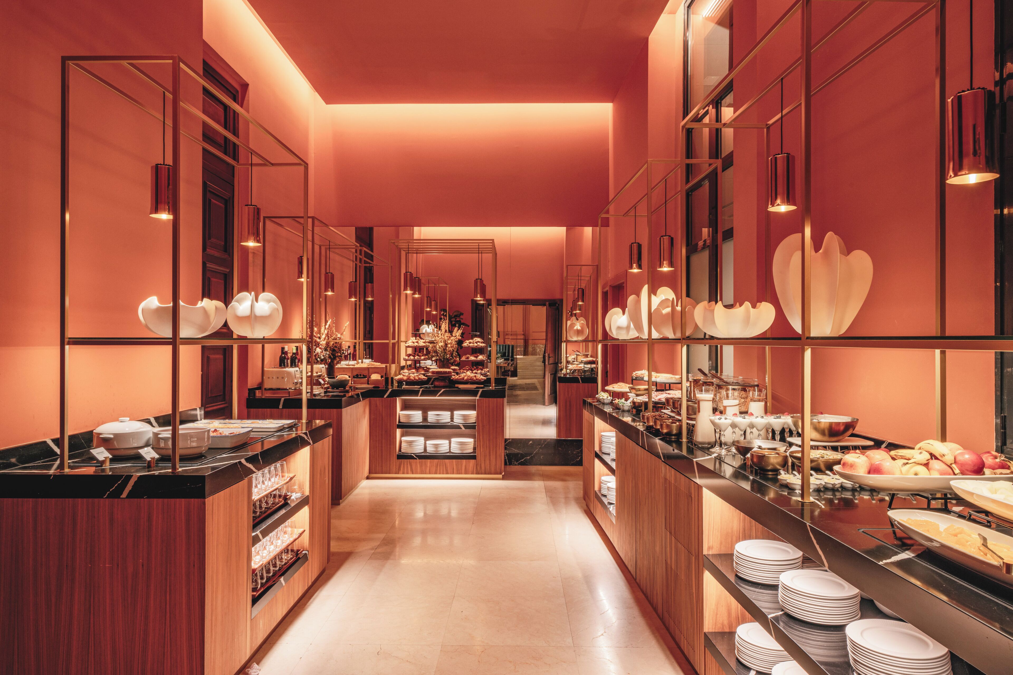 A hotel buffet with multiple food stations, a central serving area, and a long counter with plates and bowls.