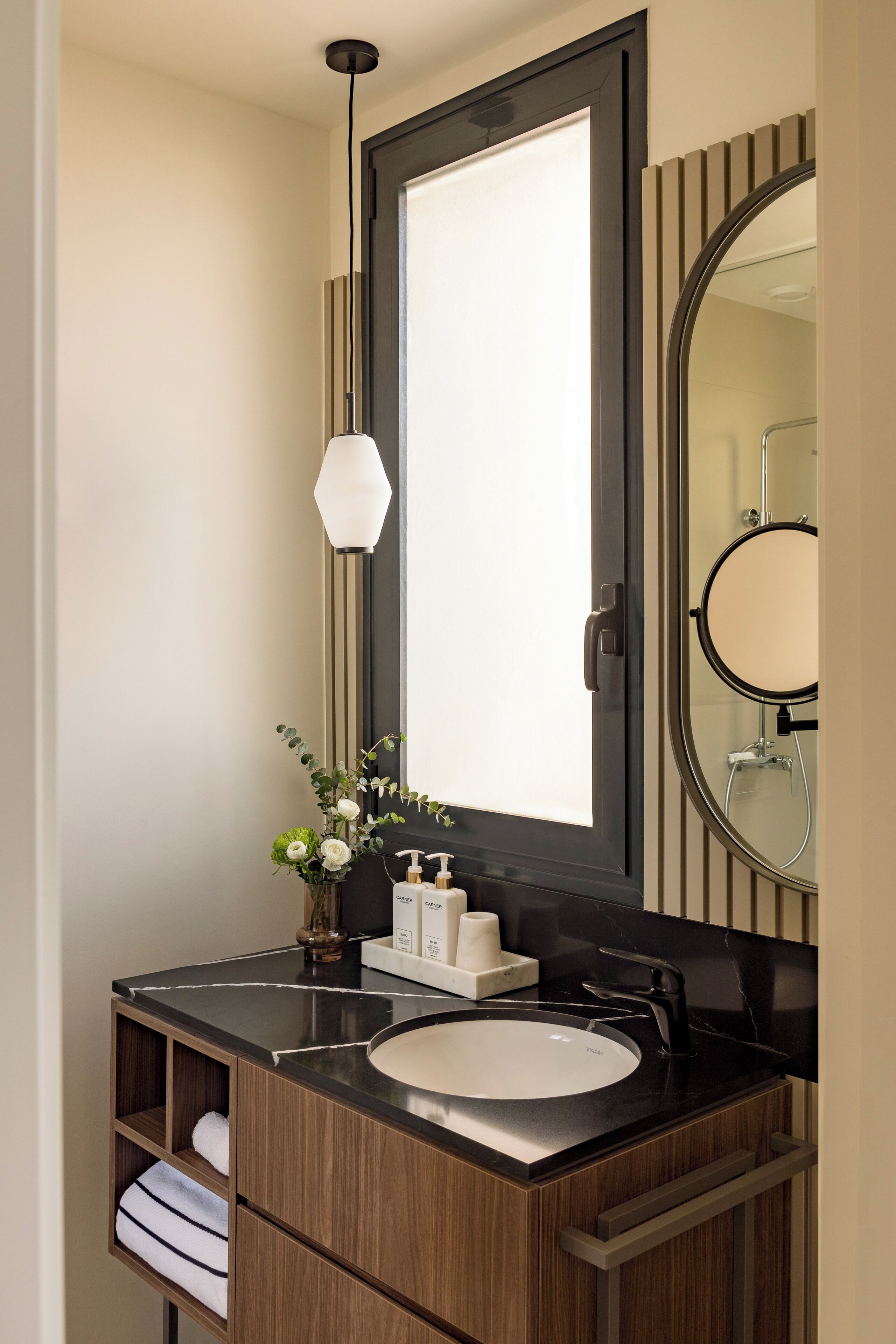 A modern bathroom with a large mirror, a round mirror, a black countertop, a white sink, and a pendant light.