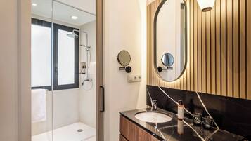 Un baño moderno con cabina de ducha de vidrio, tocador de madera con encimera de mármol negro y un espejo grande con un fondo de panel de madera.