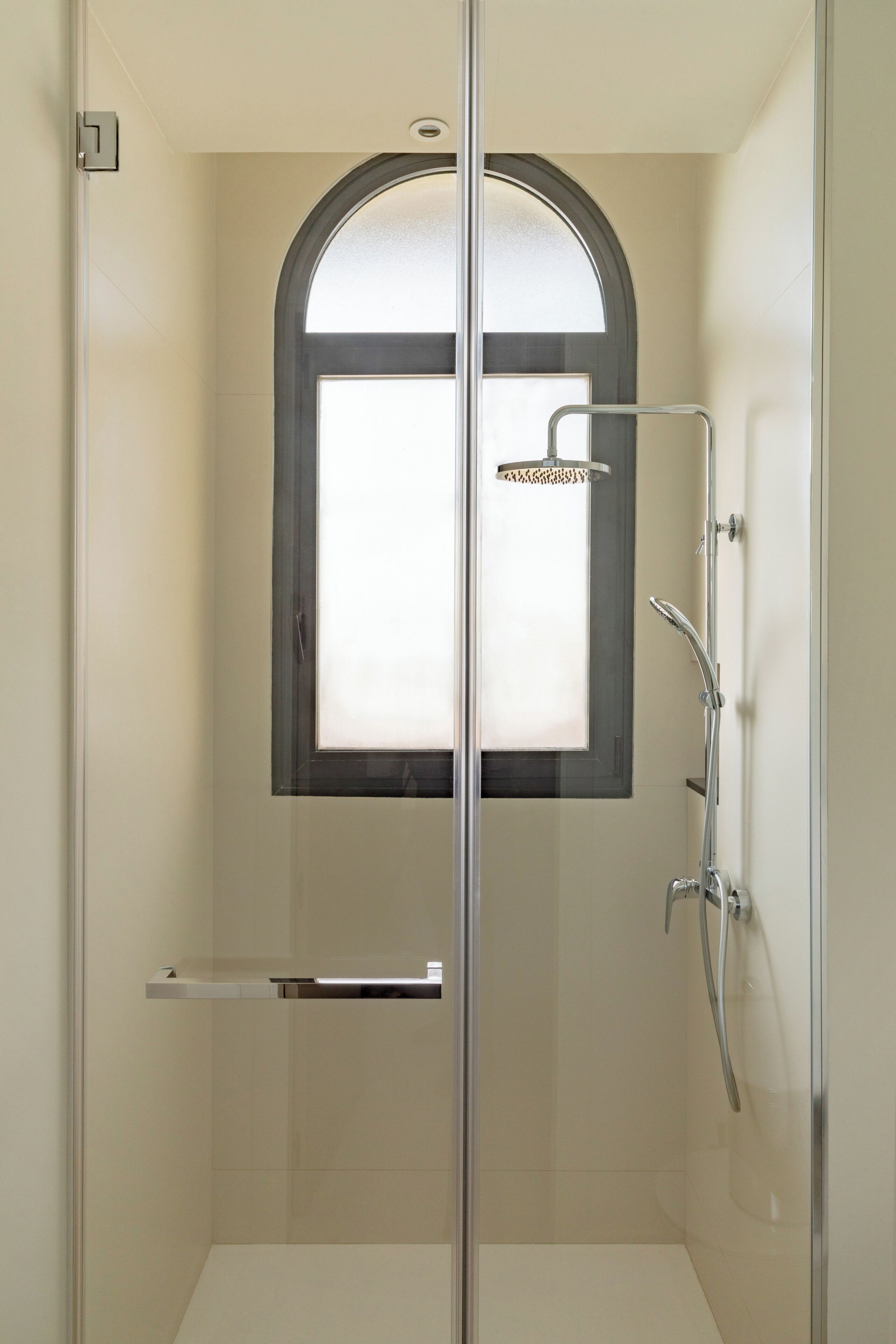 A glass-enclosed shower with a frosted window, a handheld showerhead, and a wall-mounted faucet.