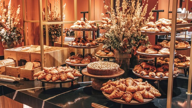 Una vitrina de panadería con diversos pasteles y pan, dispuestas sobre pedestales y mesas de madera.