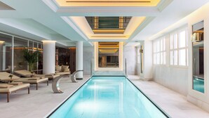 Una piscina interior moderna con áreas de descanso, techo de vidrio y suelo de mármol.