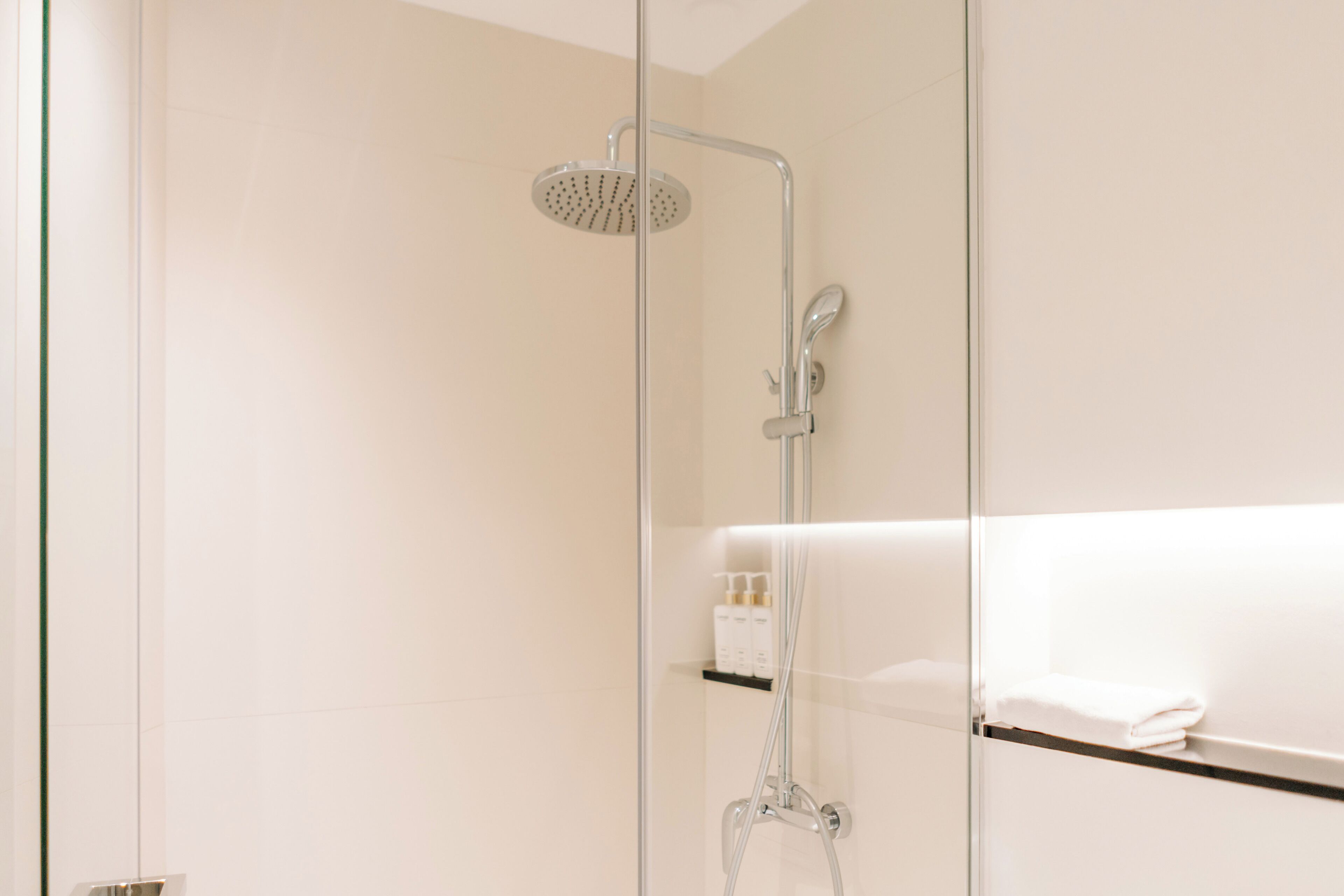 Un baño moderno con cabina de ducha de vidrio, estante empotrado con artículos de aseo y una toalla blanca en un estante.