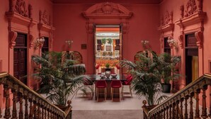 Un salón majestuoso con una mesa central, paredes rojas y columnas decorativas.
