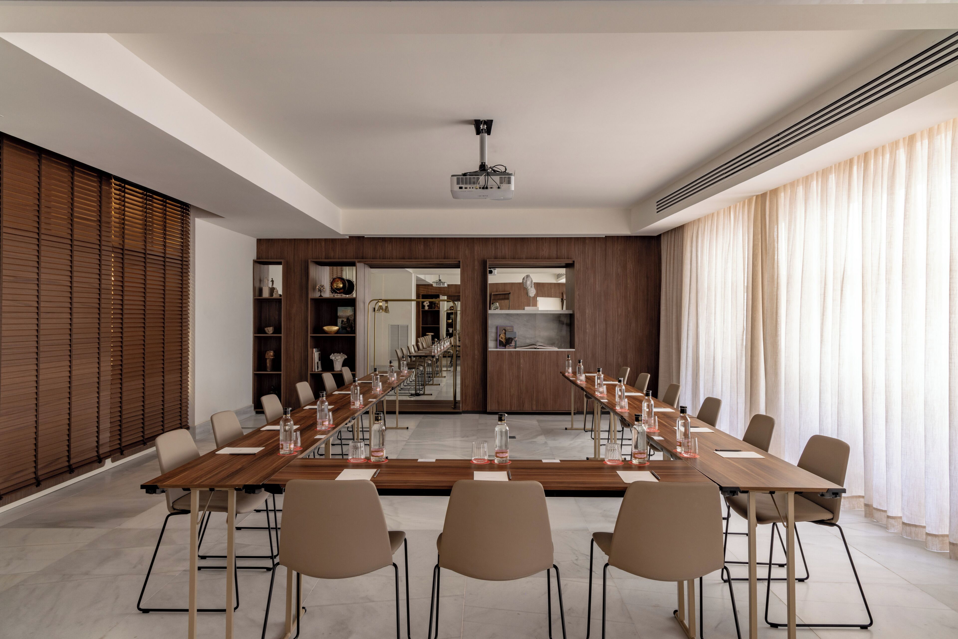 Une salle de conférence équipée d’une longue table, de chaises, d’un projecteur et offrant une vue sur un espace cuisine.