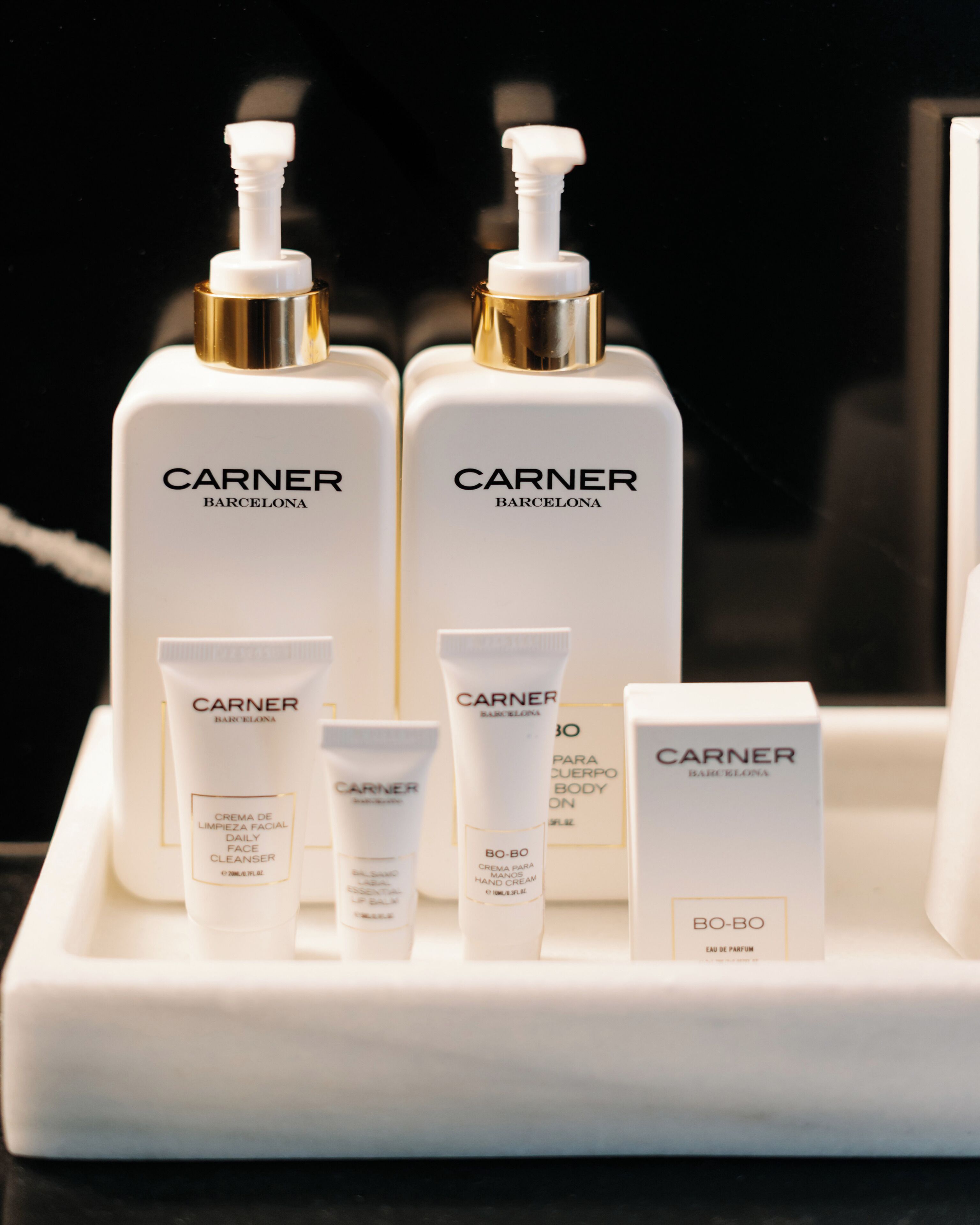 Un conjunto de productos para el cuidado de la piel de la marca CARNER, que incluye un limpiador facial, crema de manos y perfume, dispuestos sobre una bandeja blanca.