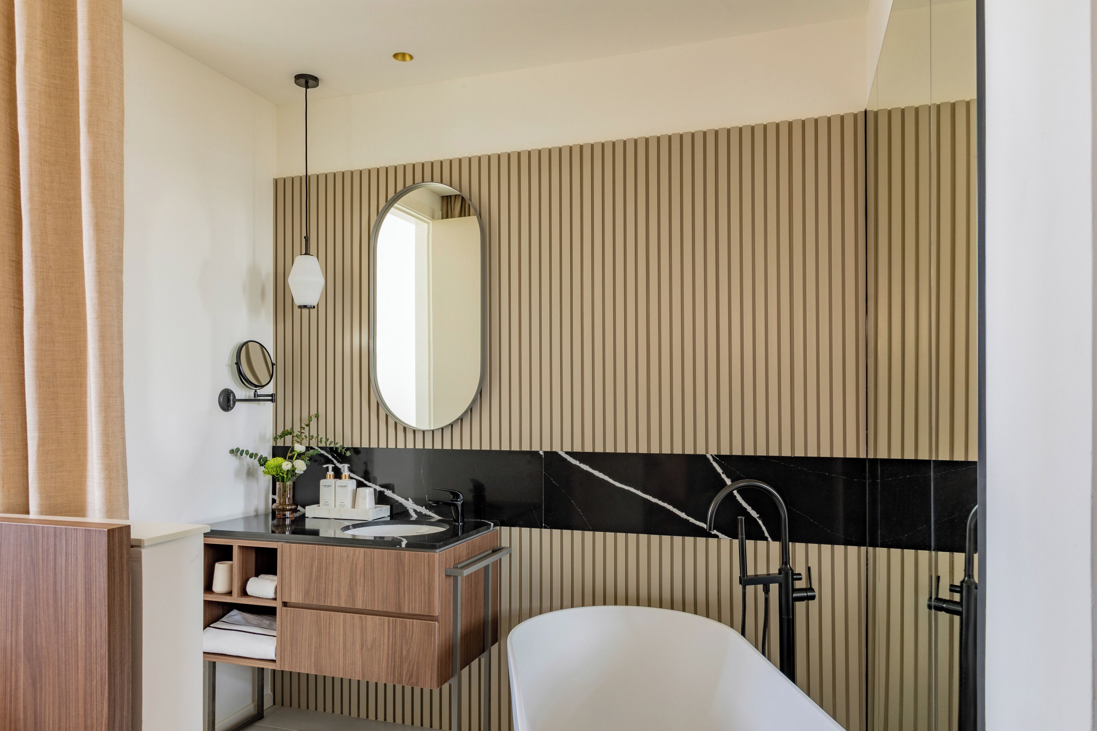 Une salle de bain moderne avec un meuble-lavabo en bois, un grand miroir, un mur recouvert de carreaux noirs et blancs, et une baignoire blanche.